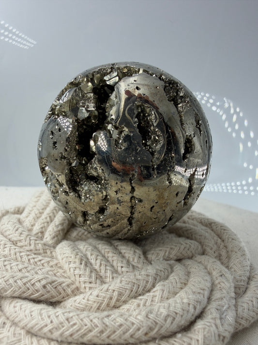 Eine hochglänzende, metallisch Pyrit-Kugel, deren spiegelnde Oberfläche die Umgebung reflektiert und winzige, natürliche Kristallstrukturen offenbart.