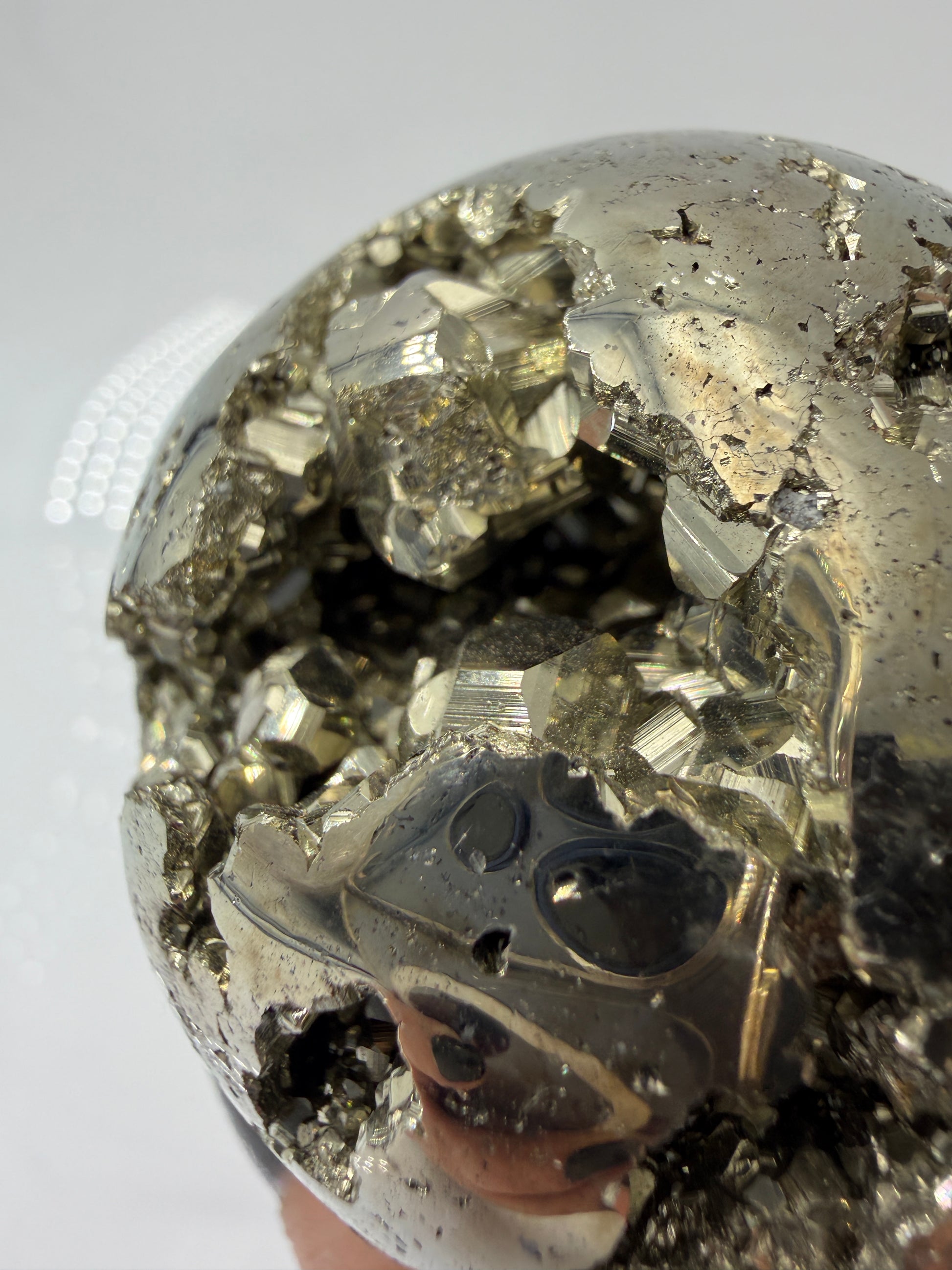Eine hochglänzende, metallisch Pyrit-Kugel, deren spiegelnde Oberfläche die Umgebung reflektiert und winzige, natürliche Kristallstrukturen offenbart.