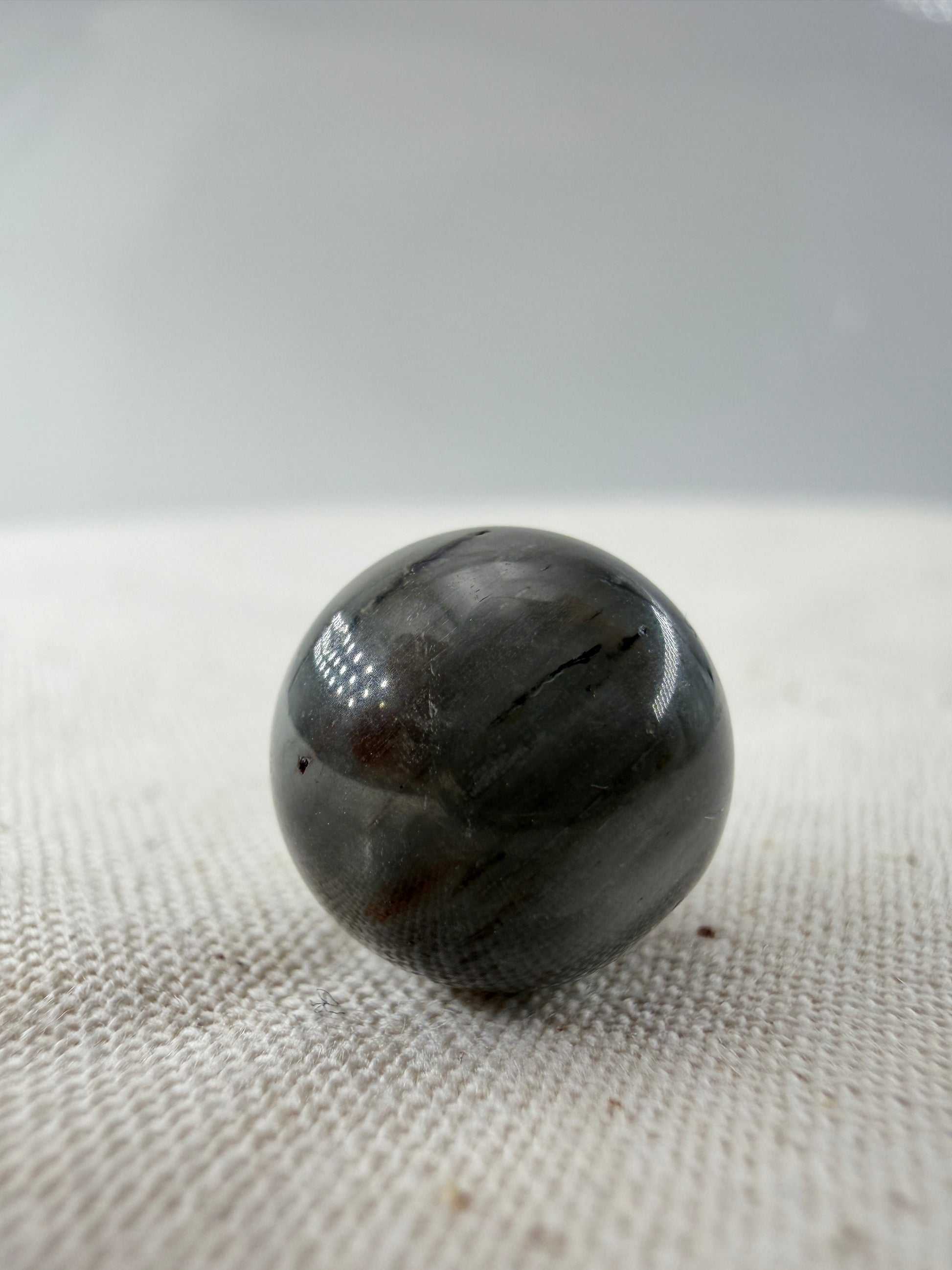 Rabbit Hair Minikugel aus Quarz mit grauen nadelförmigen Mineraleinschlüssen, Ø 1,1–1,3 cm.