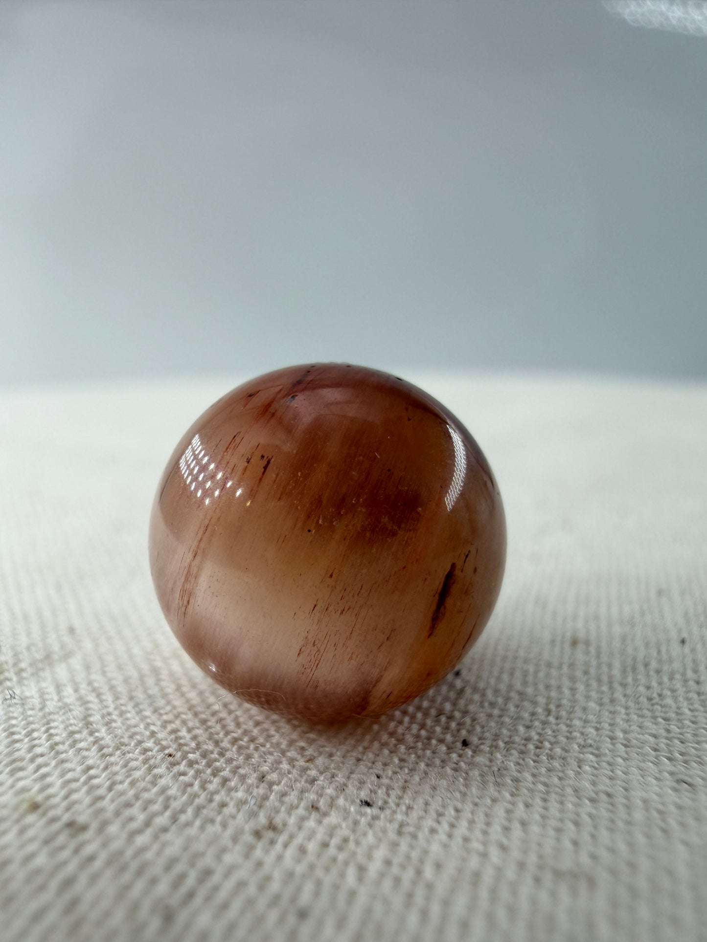 Rabbit Hair Minikugel aus Quarz mit roten nadelförmigen Mineraleinschlüssen, Ø 1,1–1,3 cm.