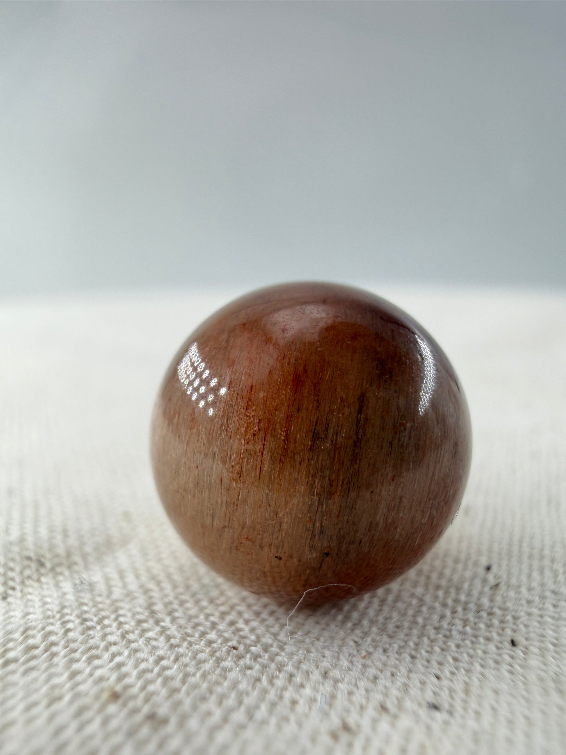 Rabbit Hair Minikugel aus Quarz mit roten nadelförmigen Mineraleinschlüssen, Ø 1,1–1,3 cm.