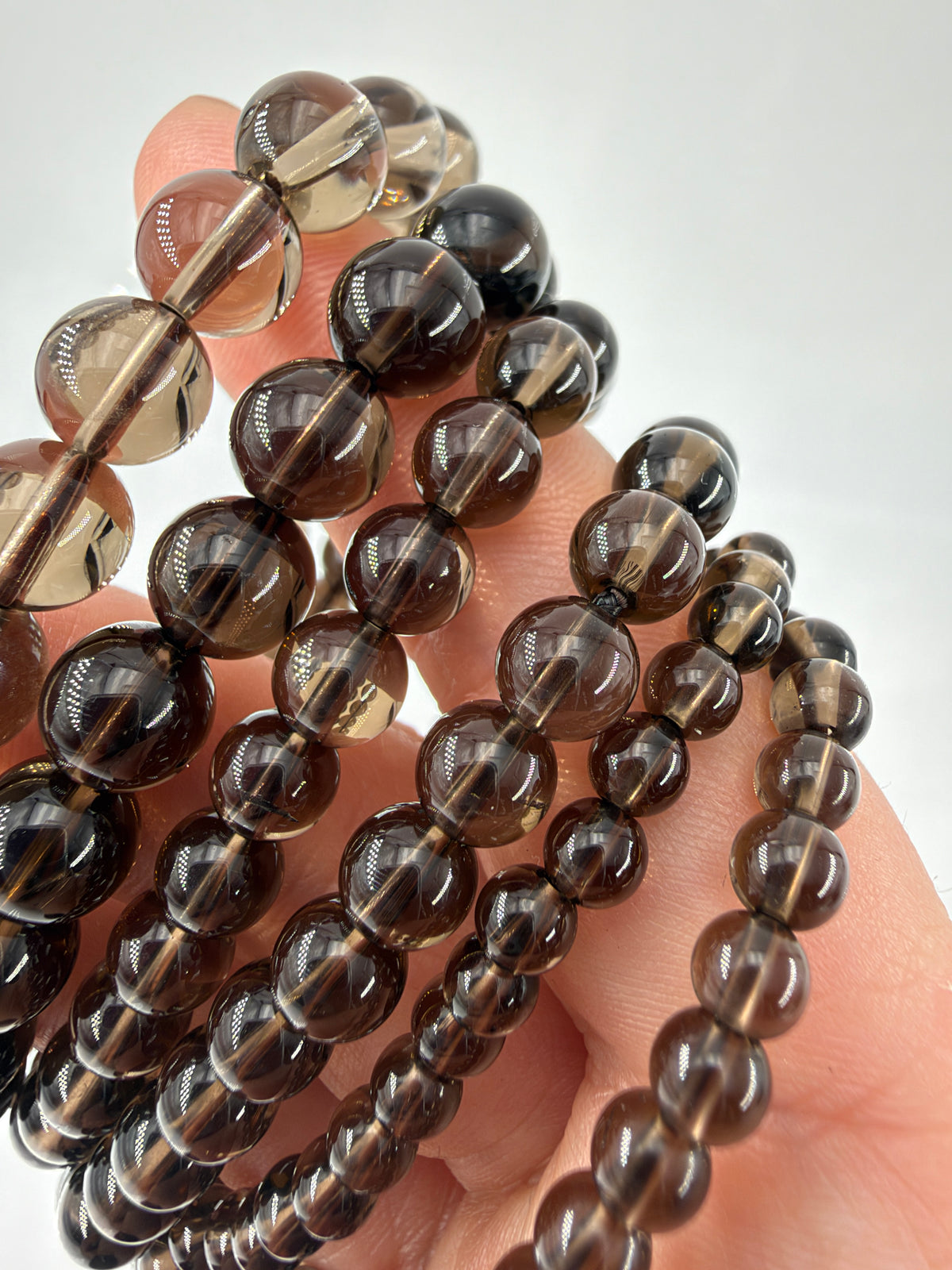 Nahaufnahme durchscheinender, rauchbrauner Kugelperlen der Rauchquarz-Armbänder, über Finger gelegt.
