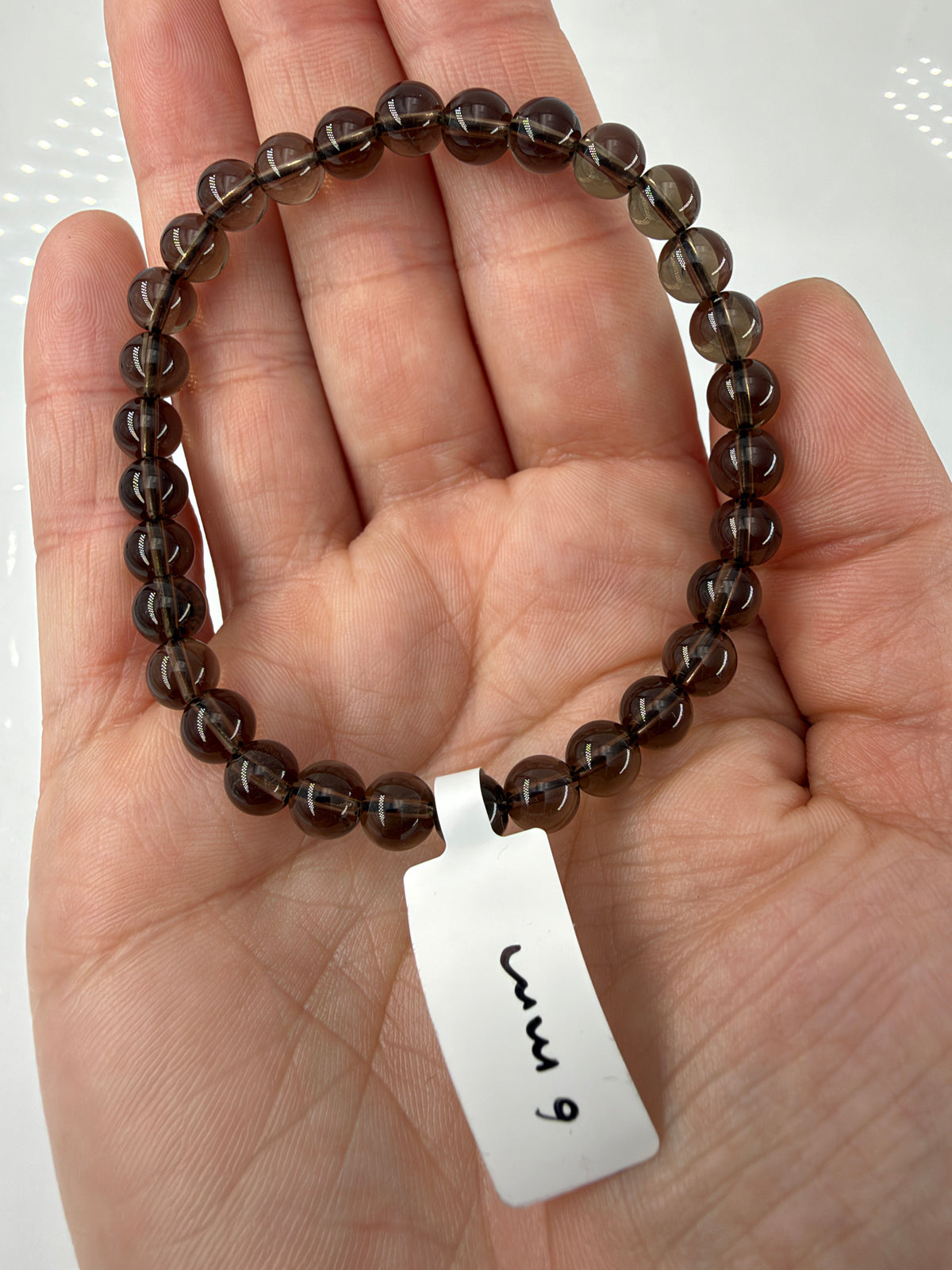 Rauchquarz-Armband RA10 mit braunen 6-mm-Kugelperlen auf einer offenen Hand.