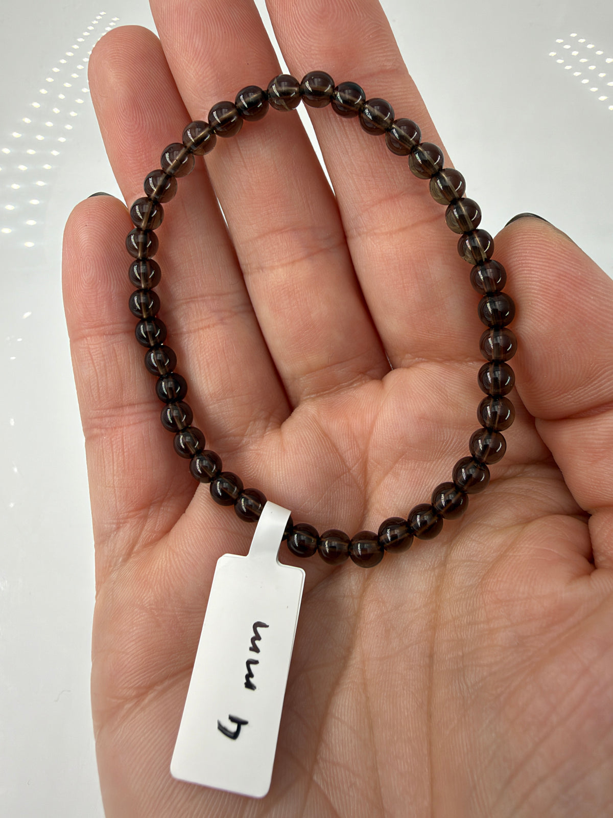Rauchquarz-Armband RA8 mit braunen 4-mm-Kugelperlen auf einer offenen Hand.