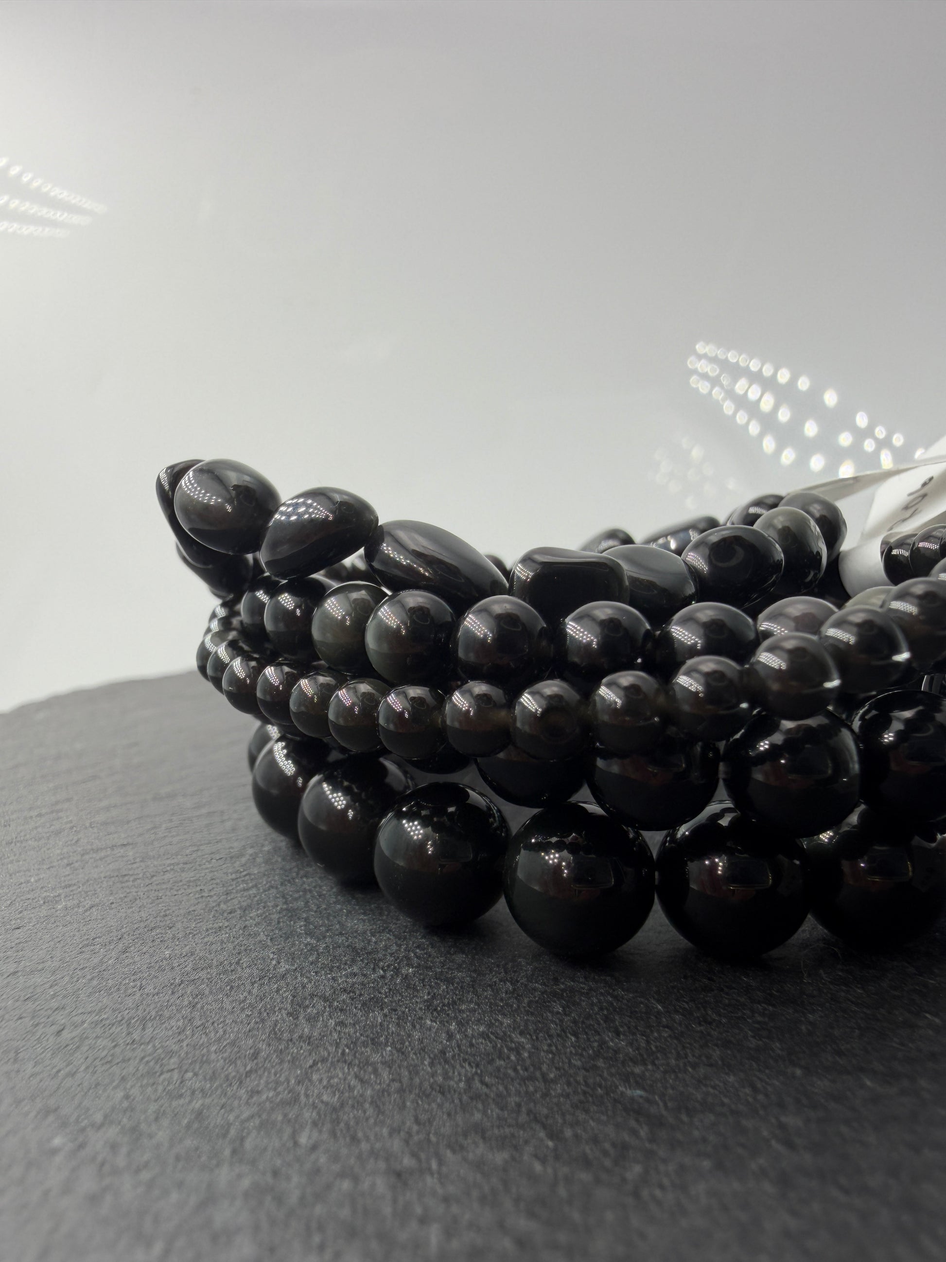 Kugelarmband aus Regenbogen-Obsidian mit irisierenden Farbringen in Violett und Grün.