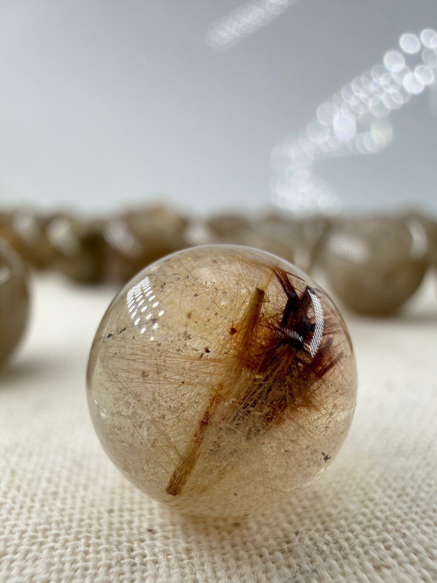 Rutil Minikugel mit seidigem Metallglanz und nadelförmigen Einschlüssen, tetragonale Kristallstruktur sichtbar, Ø ca. 1,1 cm.