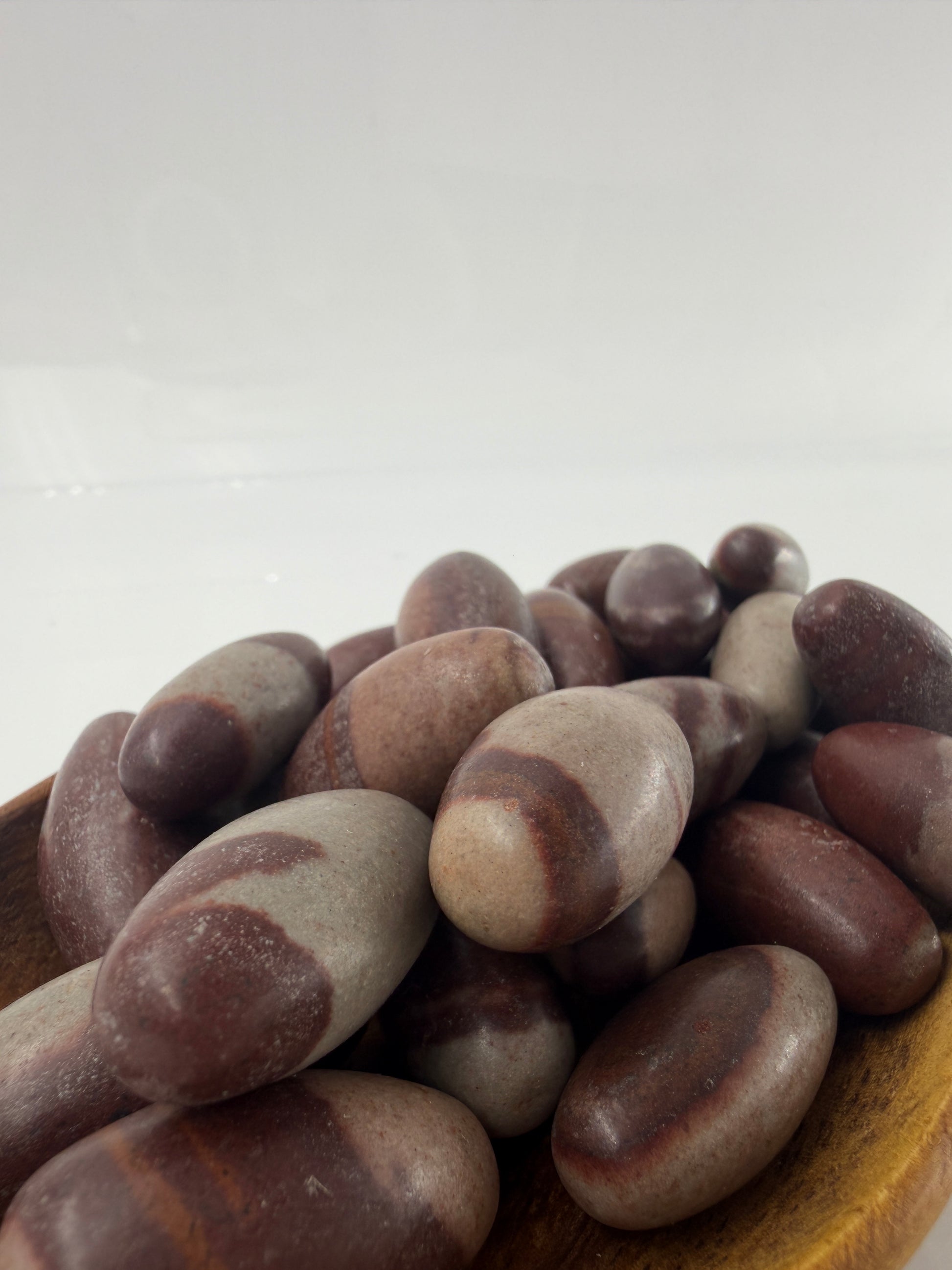 Kleiner, elliptisch geformter Shiva Lingam aus Indien mit markanter braun-roter Bänderung und glatter Oberfläche.