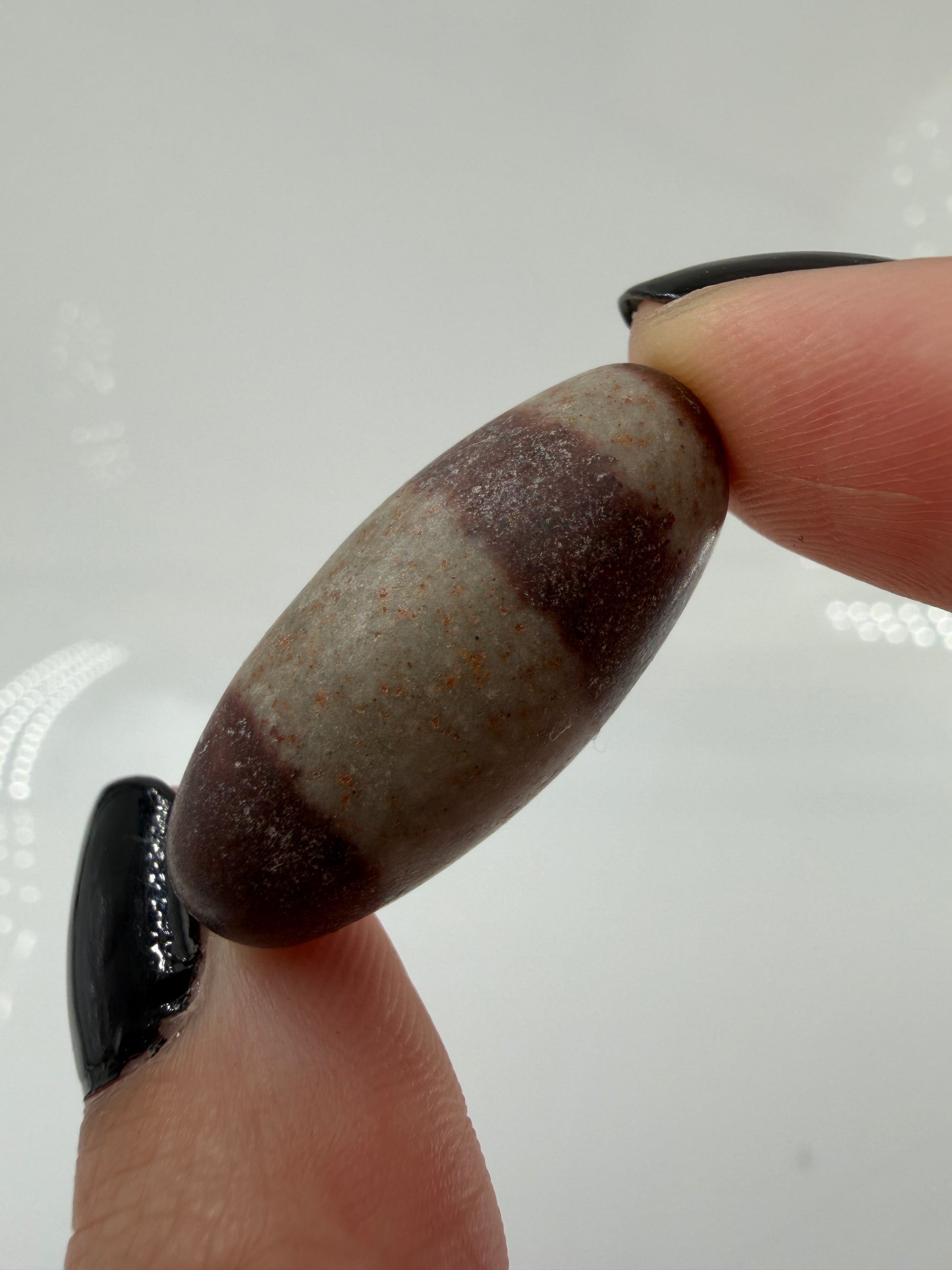Kleiner, elliptisch geformter Shiva Lingam aus Indien mit markanter braun-roter Bänderung und glatter Oberfläche.