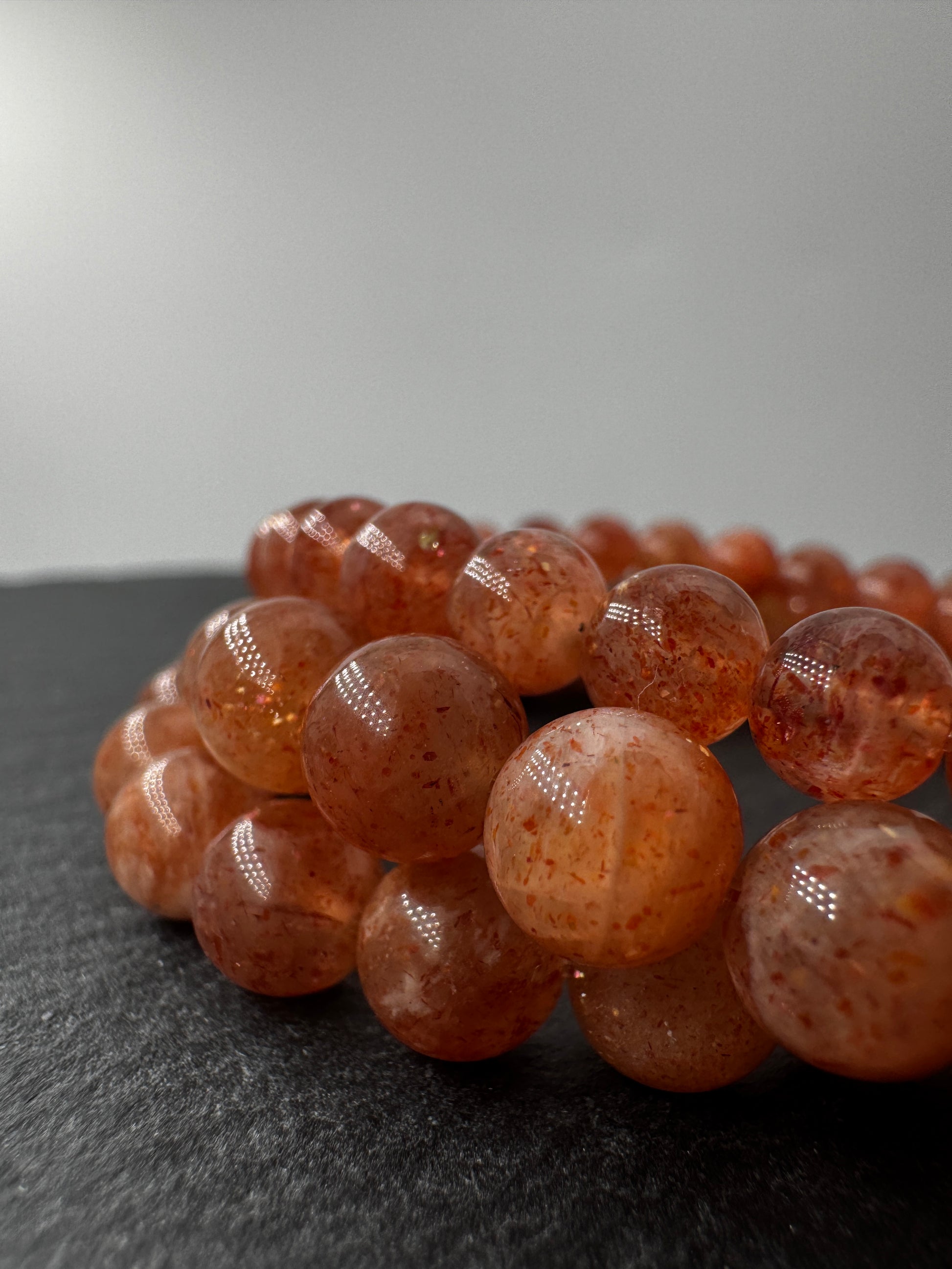 Ein glanzvolles Armband aus pfirsichfarbenen Sonnenstein-Kugeln mit feinem Goldschimmer, das sanft in der Sonne funkelt.