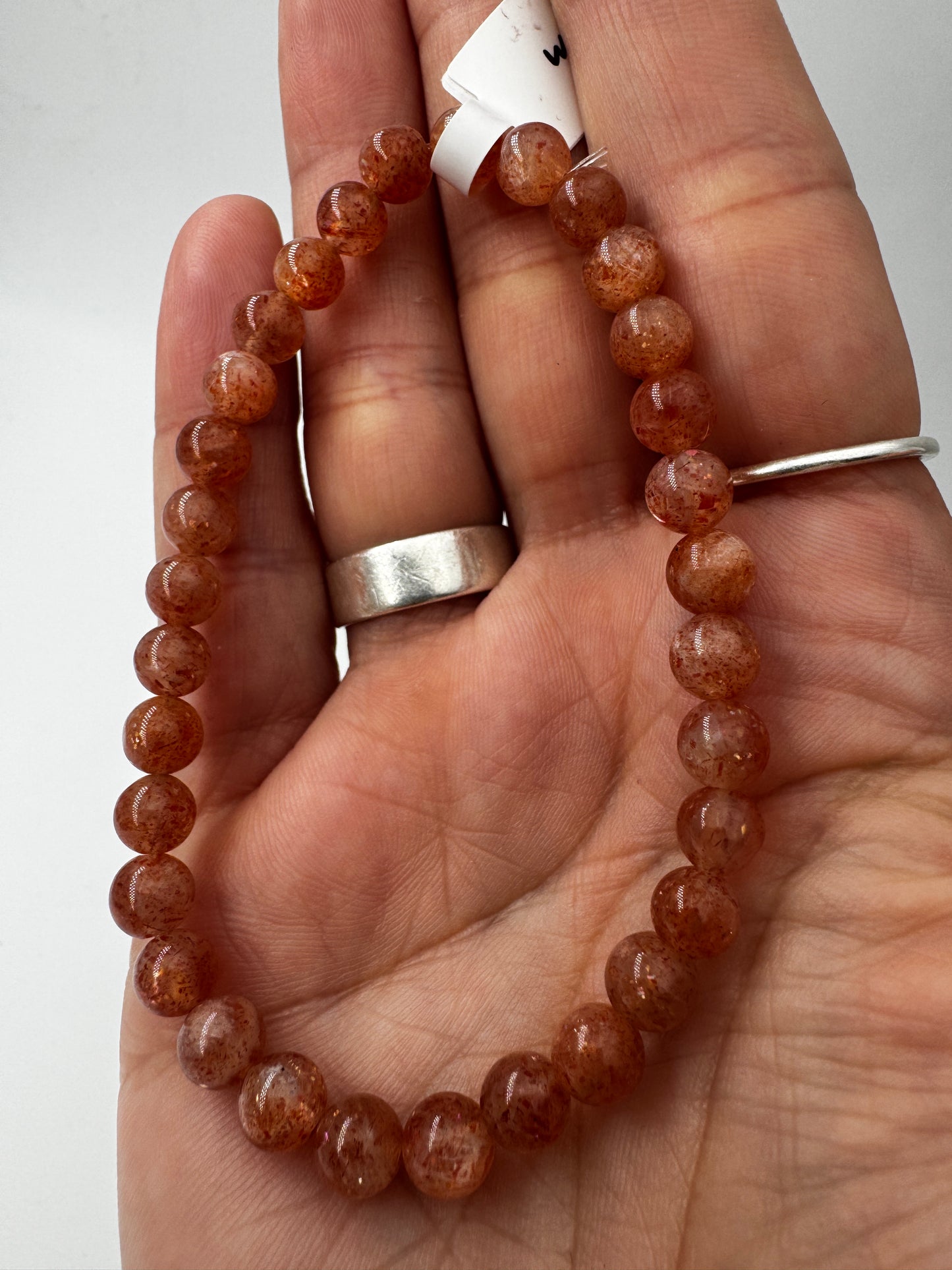 Ein glanzvolles Armband aus pfirsichfarbenen Sonnenstein-Kugeln mit feinem Goldschimmer, das sanft in der Sonne funkelt.