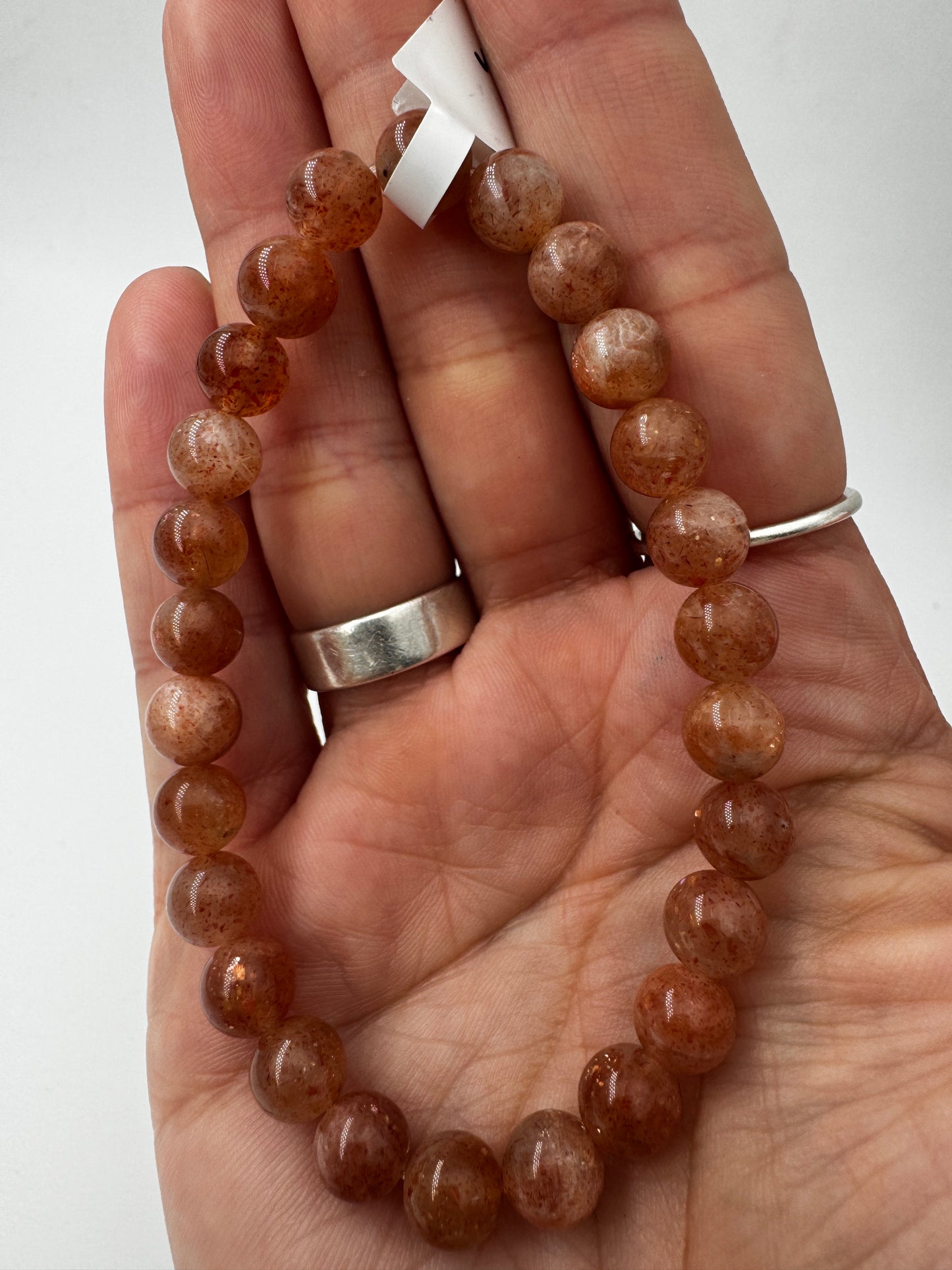 Ein glanzvolles Armband aus pfirsichfarbenen Sonnenstein-Kugeln mit feinem Goldschimmer, das sanft in der Sonne funkelt.