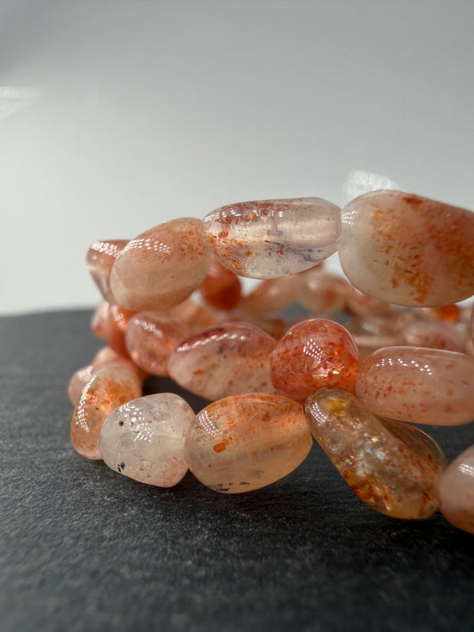 Splitterarmband aus schimmerndem Sonnenstein mit warmen Orangetönen und feinen metallischen Reflexen.