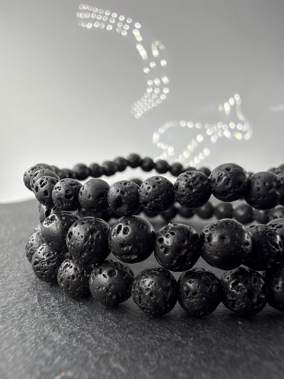 Vulkangestein-Armbänder mit schwarzen, porösen Kugelperlen in zwei Größen auf dunklem Untergrund