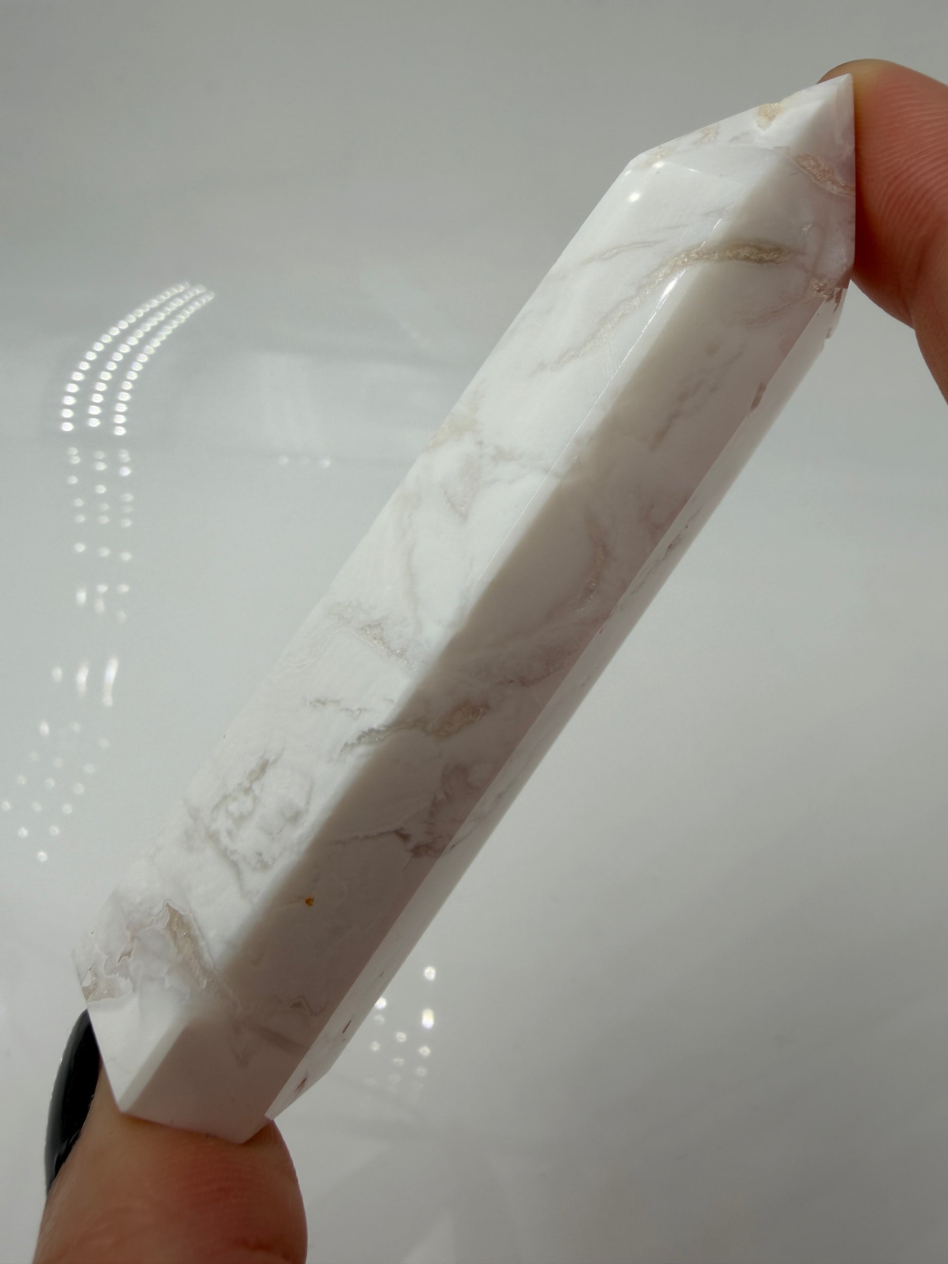 Eine geschliffene Spitze aus weißem Achat mit einer scharfen Spitze. Das Mineral zeigt zarte, wellenförmige Bänderungen in verschiedenen Weißschattierungen und eine glänzende Oberfläche, die das Licht sanft reflektiert. 