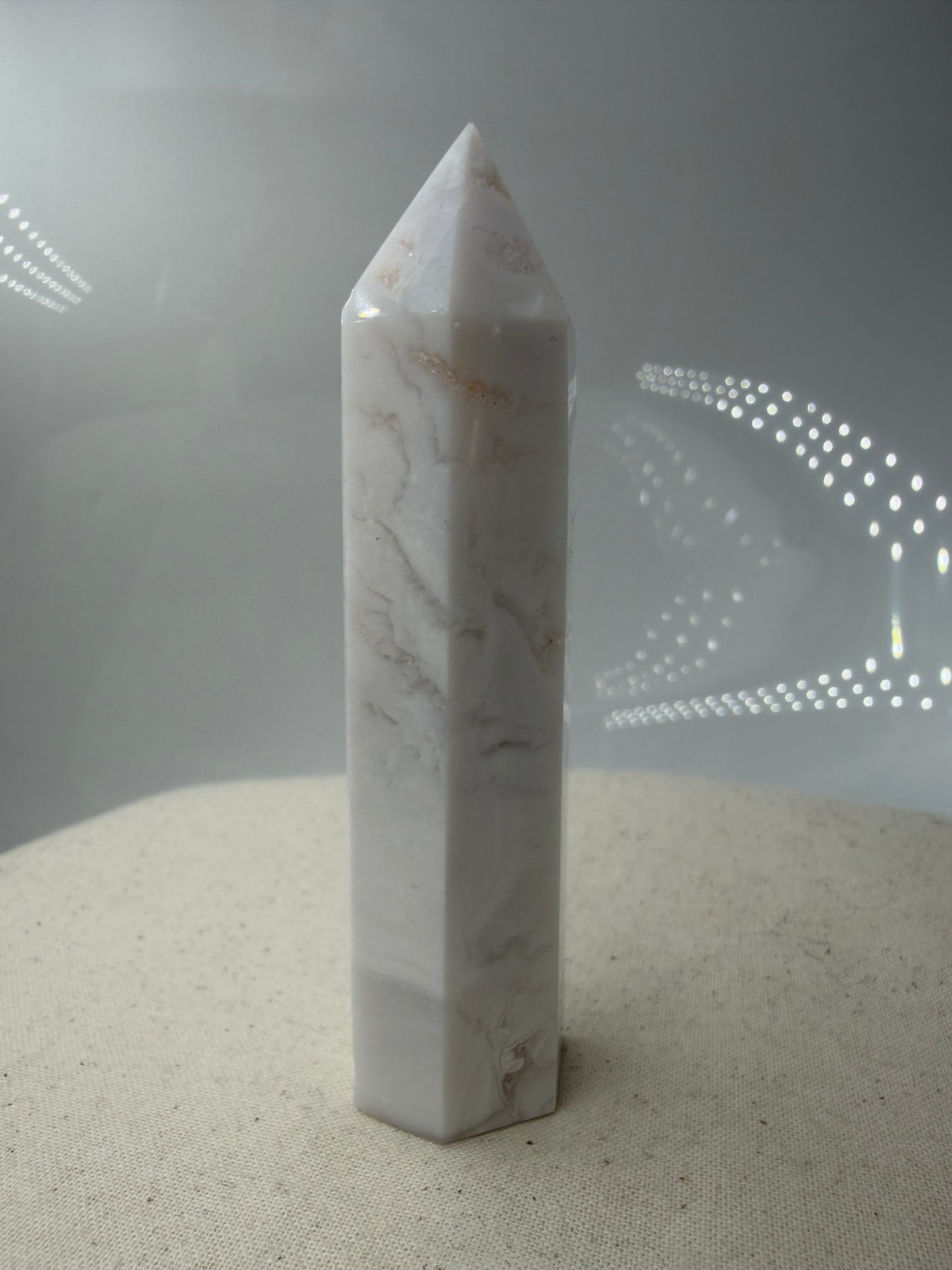 Eine geschliffene Spitze aus weißem Achat mit einer scharfen Spitze. Das Mineral zeigt zarte, wellenförmige Bänderungen in verschiedenen Weißschattierungen und eine glänzende Oberfläche, die das Licht sanft reflektiert. 