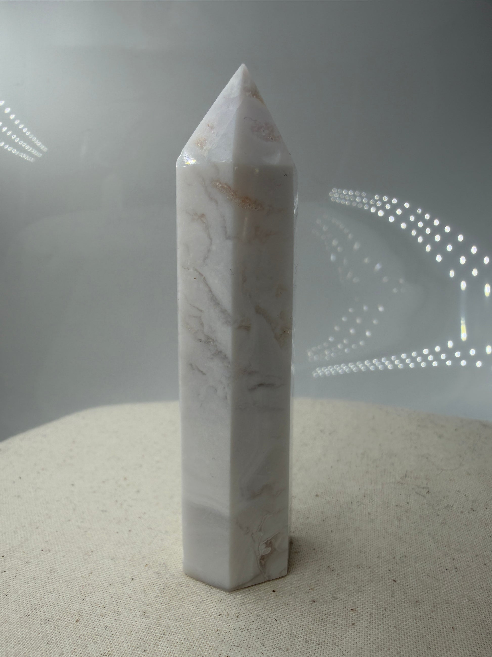 Eine geschliffene Spitze aus weißem Achat mit einer scharfen Spitze. Das Mineral zeigt zarte, wellenförmige Bänderungen in verschiedenen Weißschattierungen und eine glänzende Oberfläche, die das Licht sanft reflektiert. 