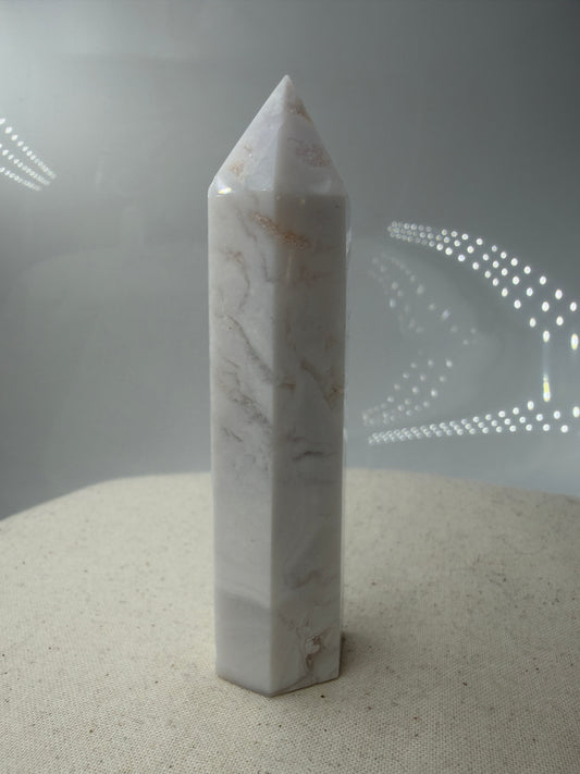 Eine geschliffene Spitze aus weißem Achat mit einer scharfen Spitze. Das Mineral zeigt zarte, wellenförmige Bänderungen in verschiedenen Weißschattierungen und eine glänzende Oberfläche, die das Licht sanft reflektiert. 