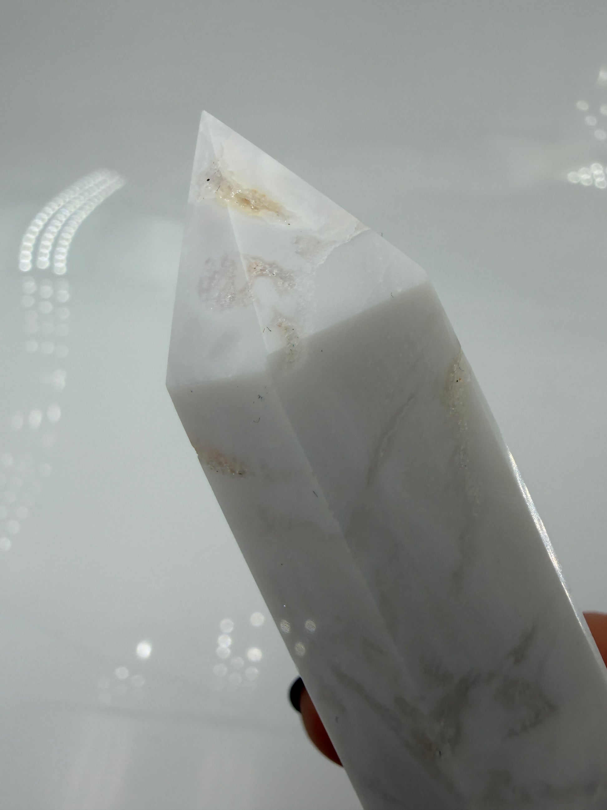 Eine geschliffene Spitze aus weißem Achat mit einer scharfen Spitze. Das Mineral zeigt zarte, wellenförmige Bänderungen in verschiedenen Weißschattierungen und eine glänzende Oberfläche, die das Licht sanft reflektiert. 
