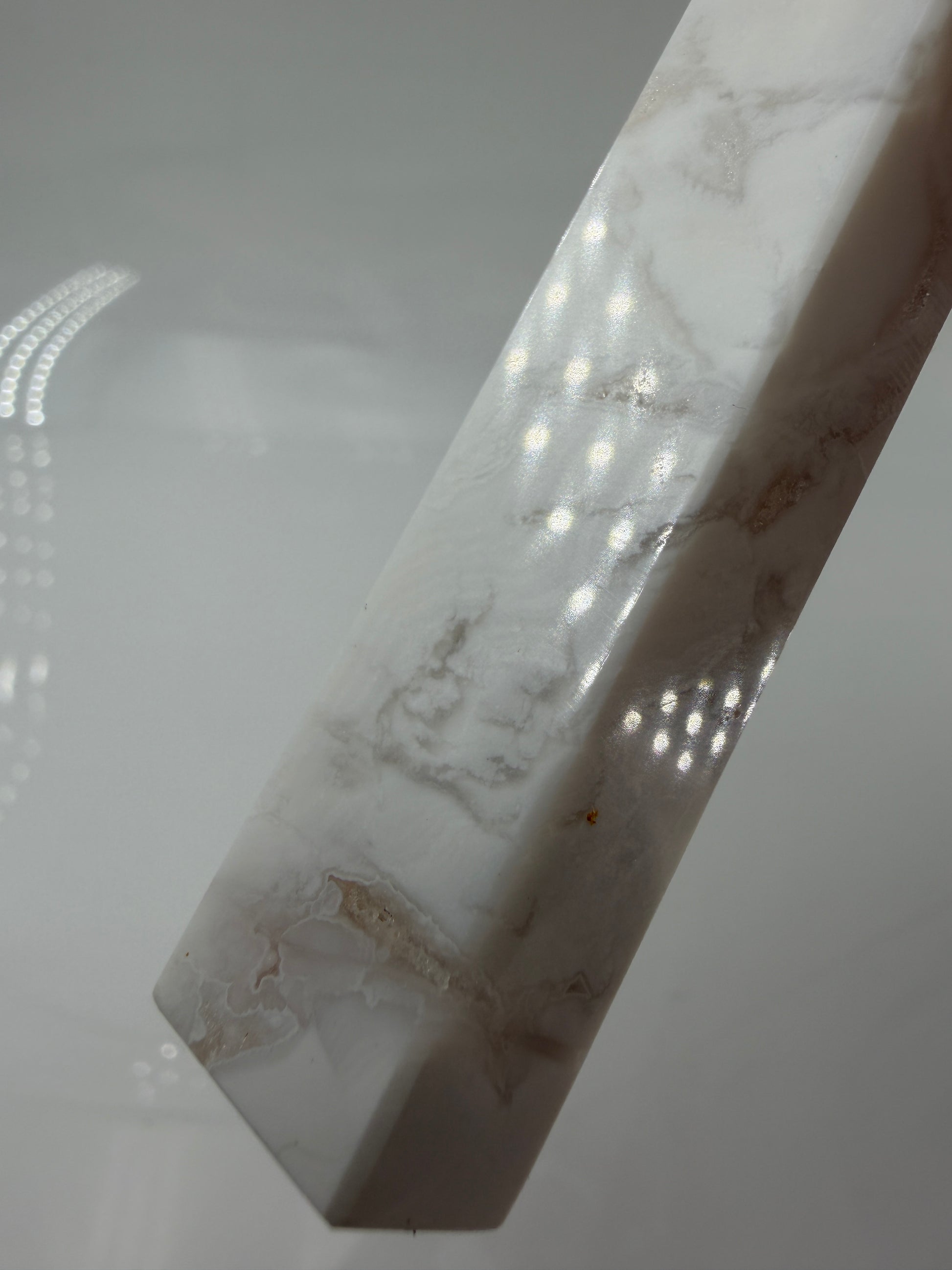 Eine geschliffene Spitze aus weißem Achat mit einer scharfen Spitze. Das Mineral zeigt zarte, wellenförmige Bänderungen in verschiedenen Weißschattierungen und eine glänzende Oberfläche, die das Licht sanft reflektiert. 