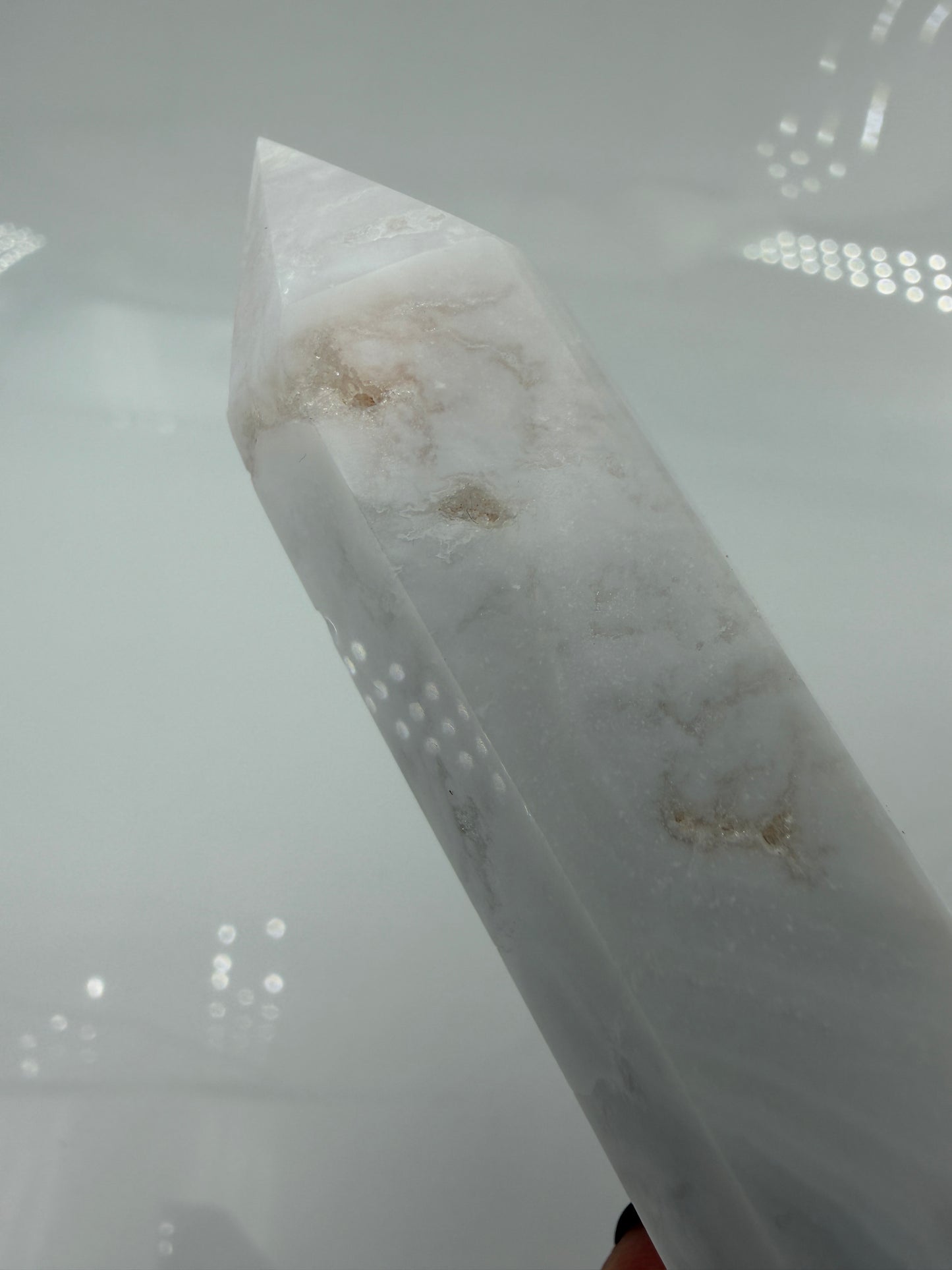 Eine geschliffene Spitze aus weißem Achat mit einer scharfen Spitze. Das Mineral zeigt zarte, wellenförmige Bänderungen in verschiedenen Weißschattierungen und eine glänzende Oberfläche, die das Licht sanft reflektiert. 
