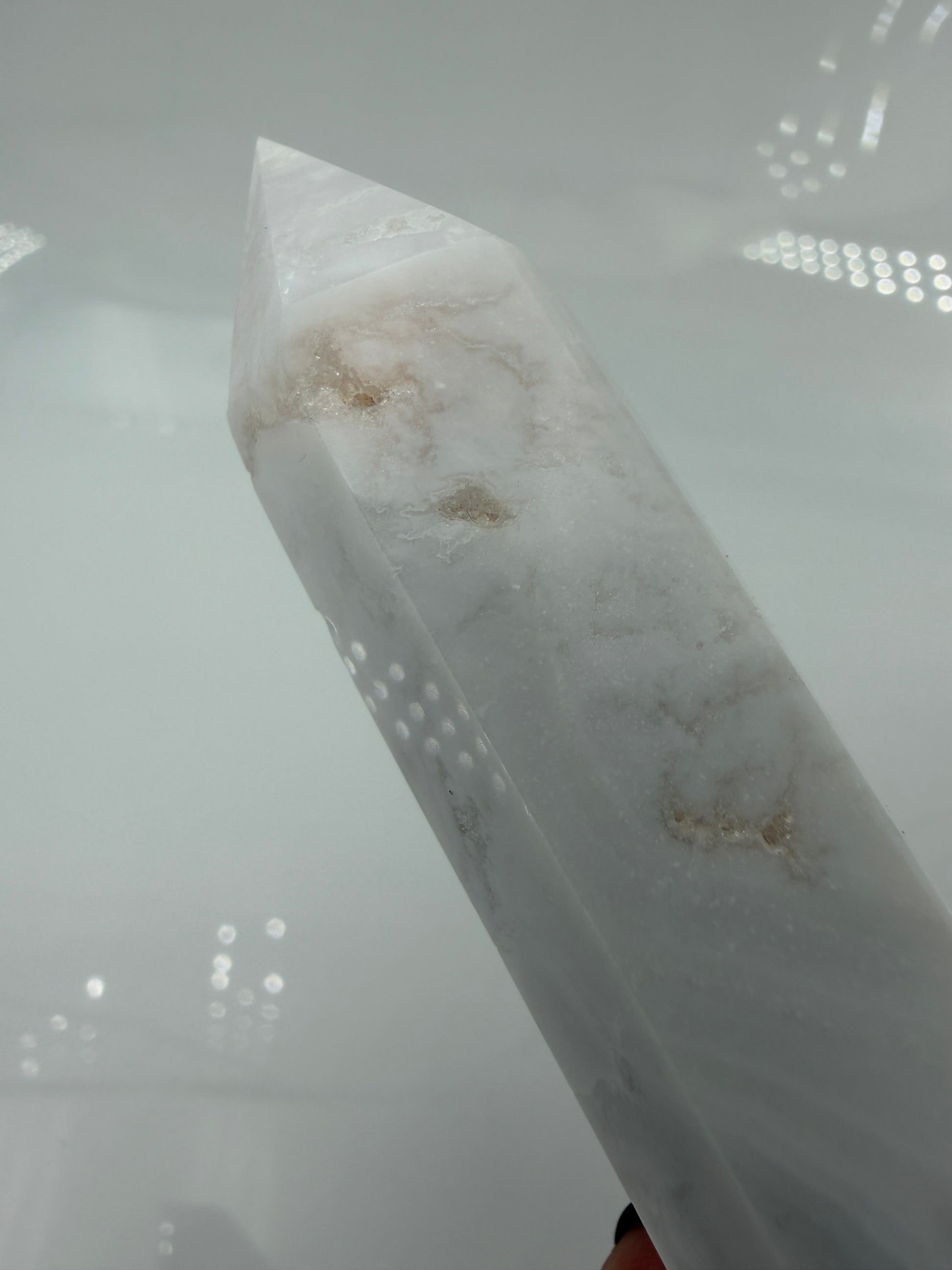 Eine geschliffene Spitze aus weißem Achat mit einer scharfen Spitze. Das Mineral zeigt zarte, wellenförmige Bänderungen in verschiedenen Weißschattierungen und eine glänzende Oberfläche, die das Licht sanft reflektiert. 