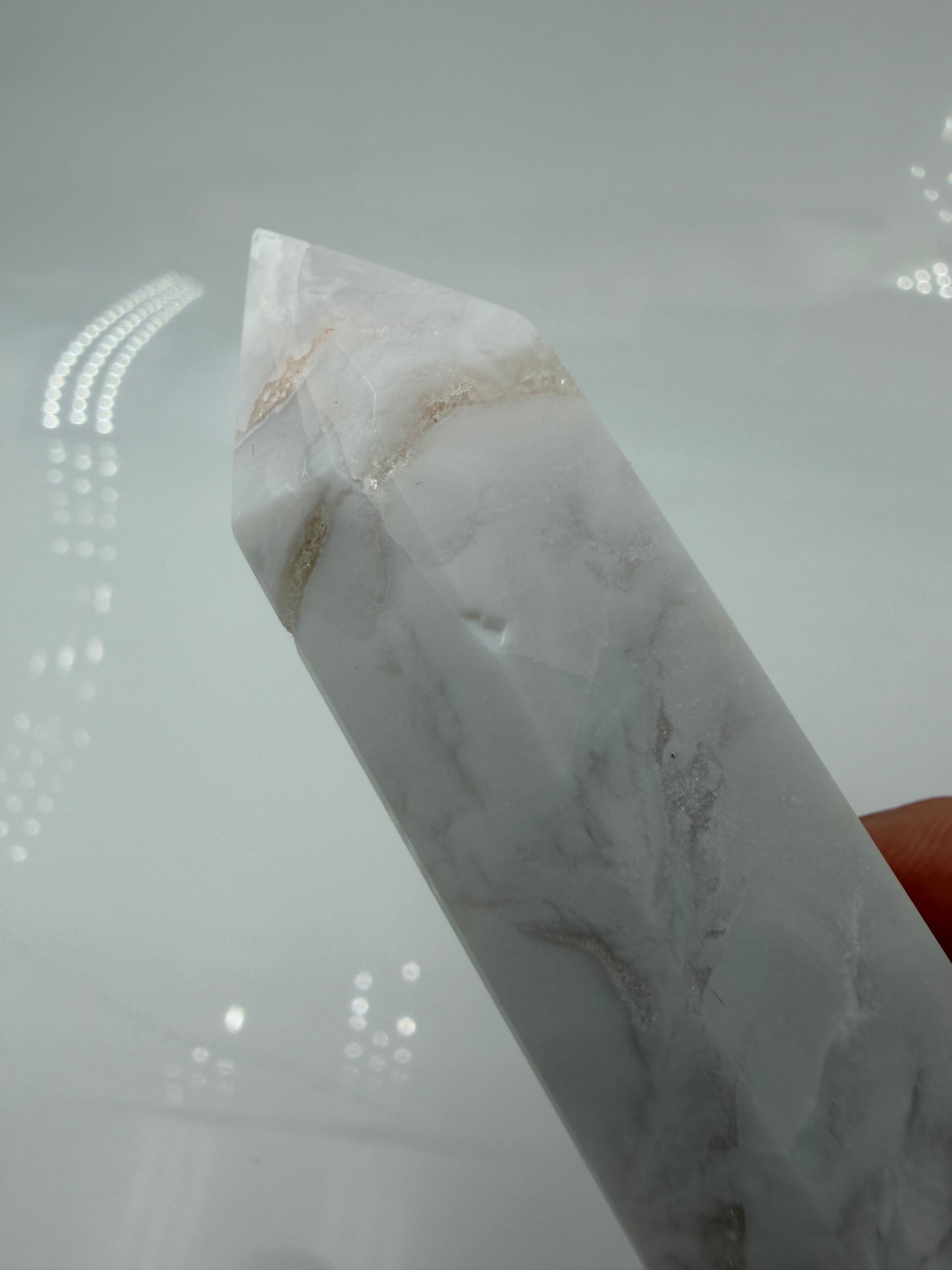 Eine geschliffene Spitze aus weißem Achat mit einer scharfen Spitze. Das Mineral zeigt zarte, wellenförmige Bänderungen in verschiedenen Weißschattierungen und eine glänzende Oberfläche, die das Licht sanft reflektiert. 
