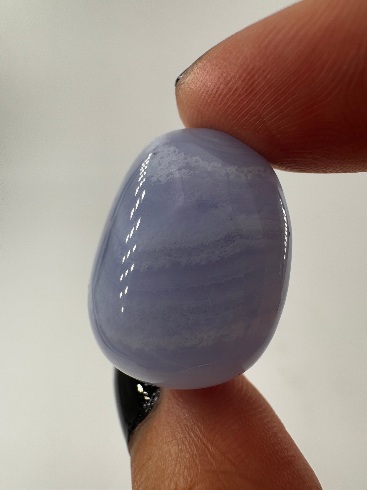 Ein Blue Lace Chalcedon Trommelstein mit seiner charakteristisch hellblauen Bänderung mit feinen weißen Linien und Wölkchen.