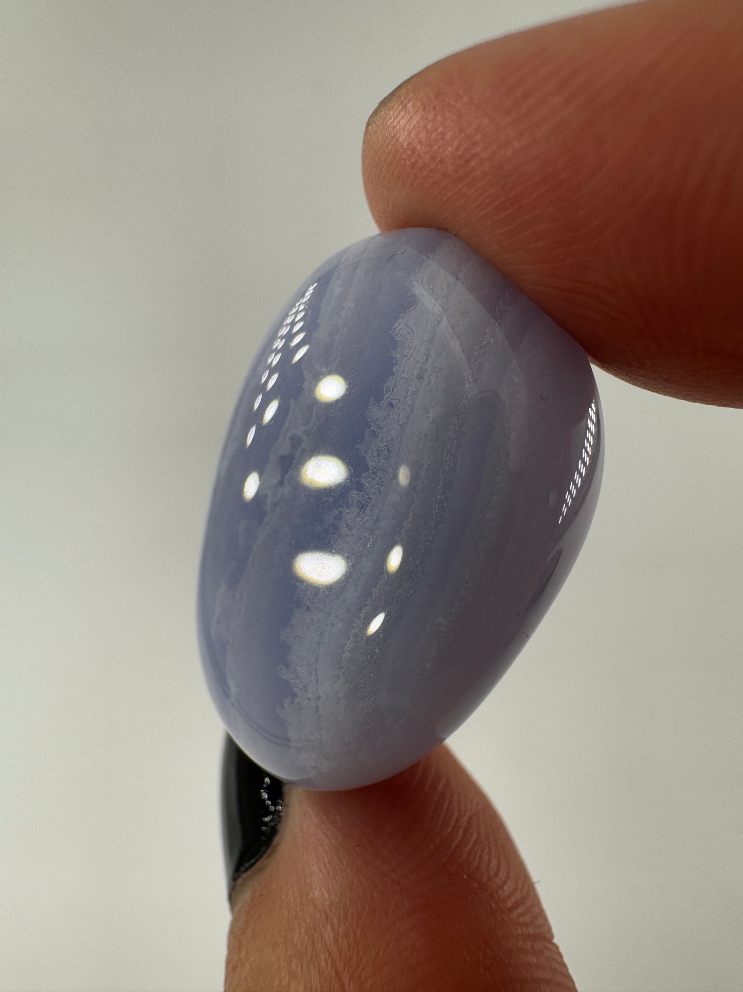Ein Blue Lace Chalcedon Trommelstein mit seiner charakteristisch hellblauen Bänderung mit feinen weißen Linien und Wölkchen.
