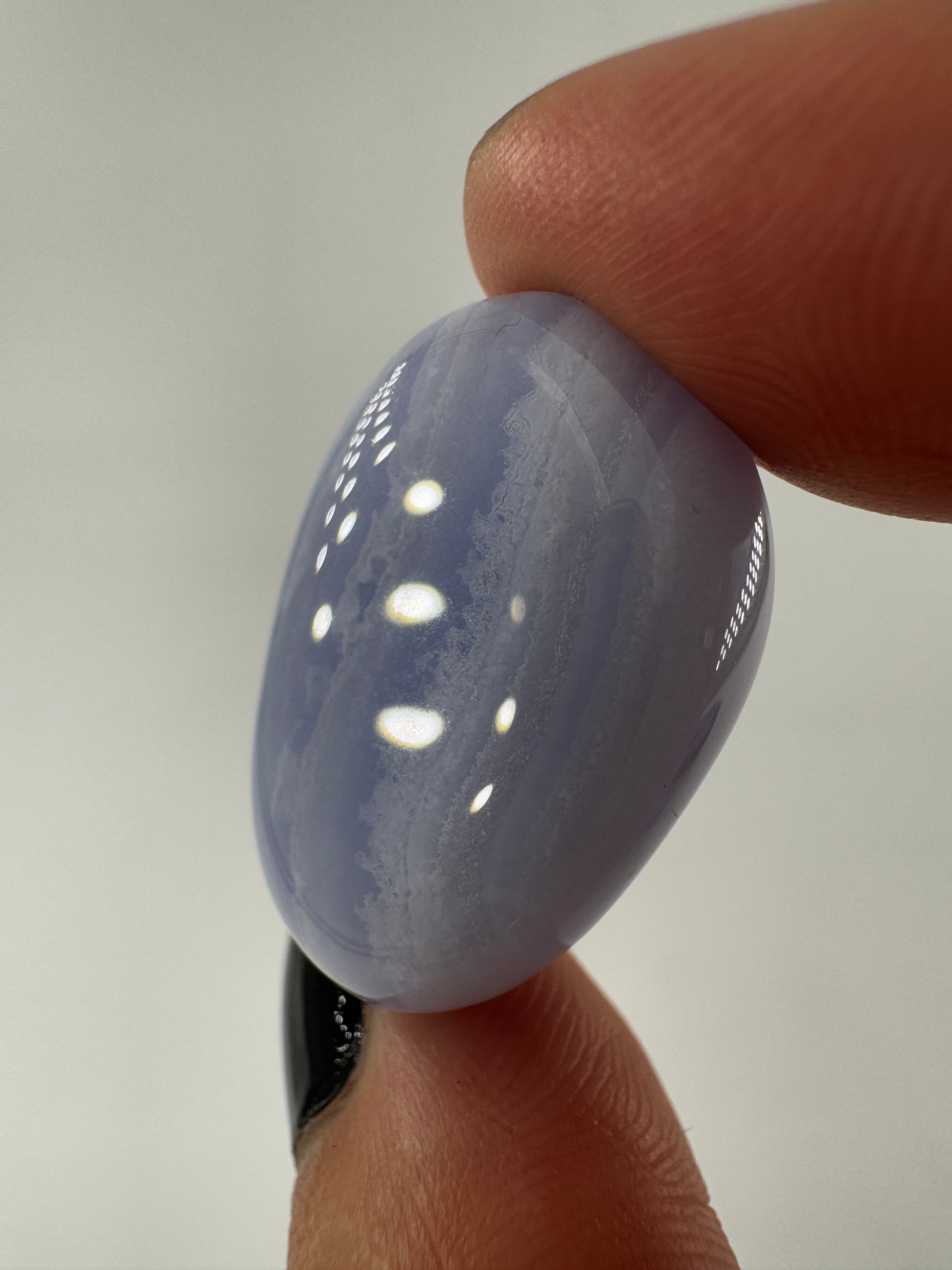 Ein Blue Lace Chalcedon Trommelstein mit seiner charakteristisch hellblauen Bänderung mit feinen weißen Linien und Wölkchen.