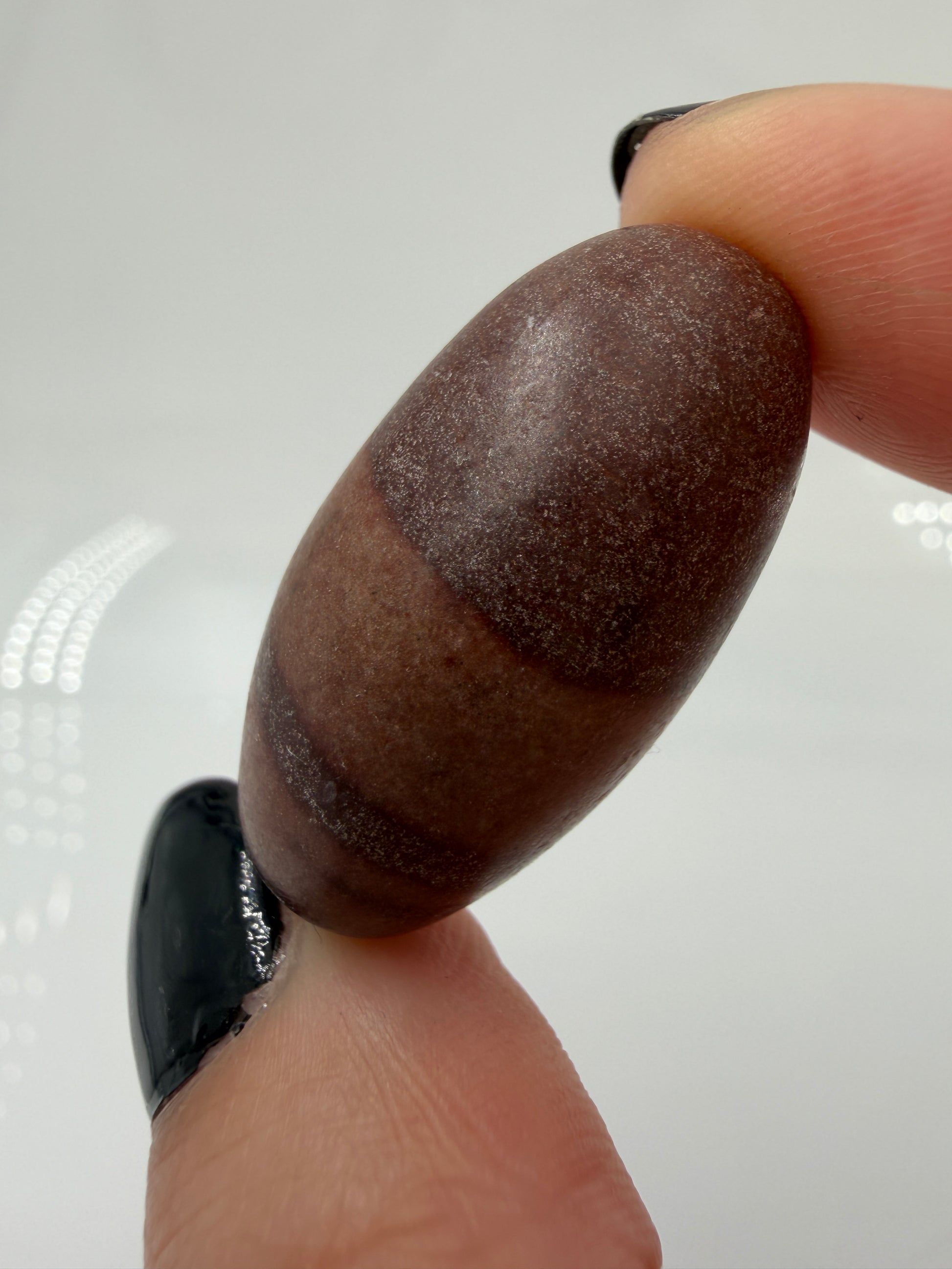 Kleiner, elliptisch geformter Shiva Lingam aus Indien mit markanter braun-roter Bänderung und glatter Oberfläche.