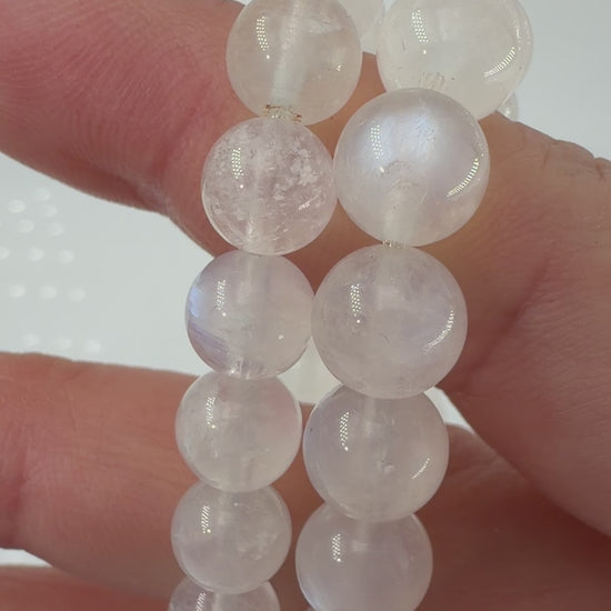 Ein elegantes Armband aus polierten, weiß-transparenten Labradorit-Kugeln, die bei Lichteinfall einen intensiven, elektrisch blauen Schimmer auf ihrer Oberfläche zeigen.