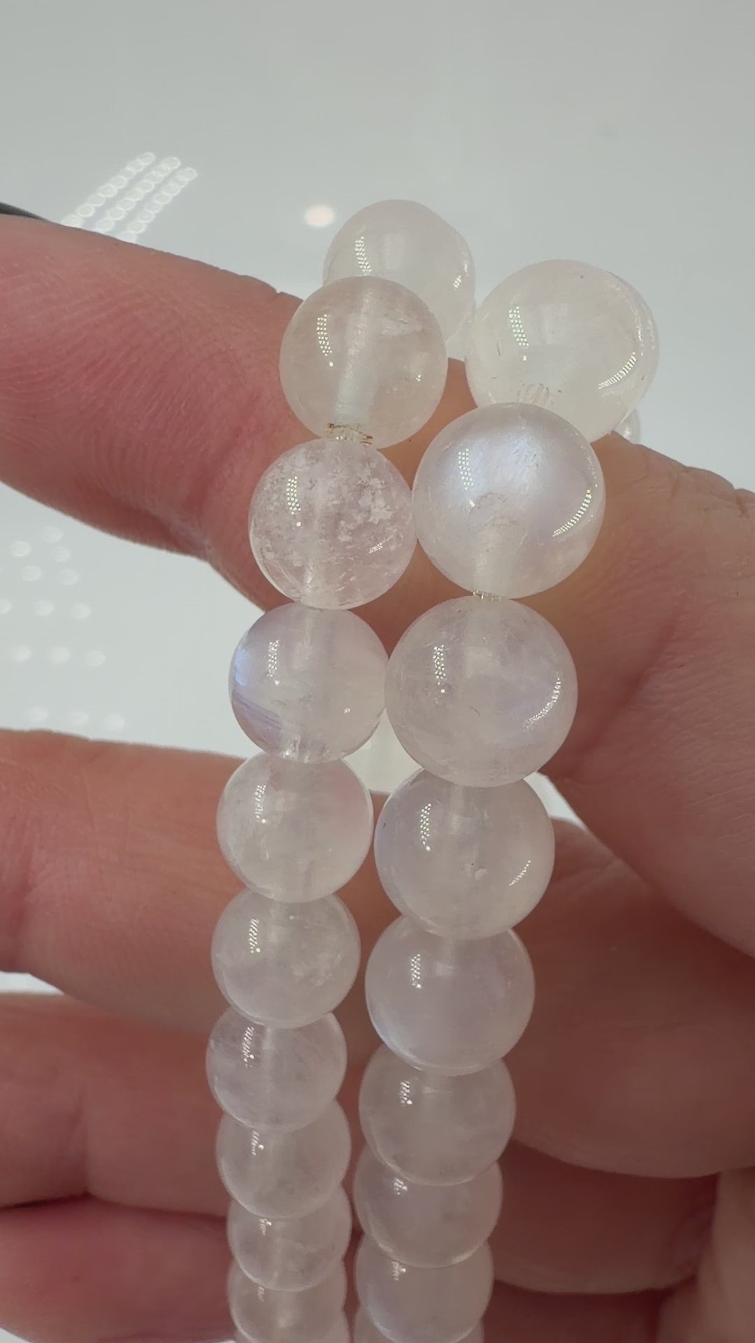 Ein elegantes Armband aus polierten, weiß-transparenten Labradorit-Kugeln, die bei Lichteinfall einen intensiven, elektrisch blauen Schimmer auf ihrer Oberfläche zeigen.