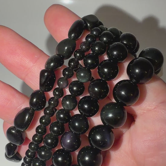 Video von den Kugelarmbändern aus Regenbogen-Obsidian mit irisierenden Farbringen in Violett und Grün.