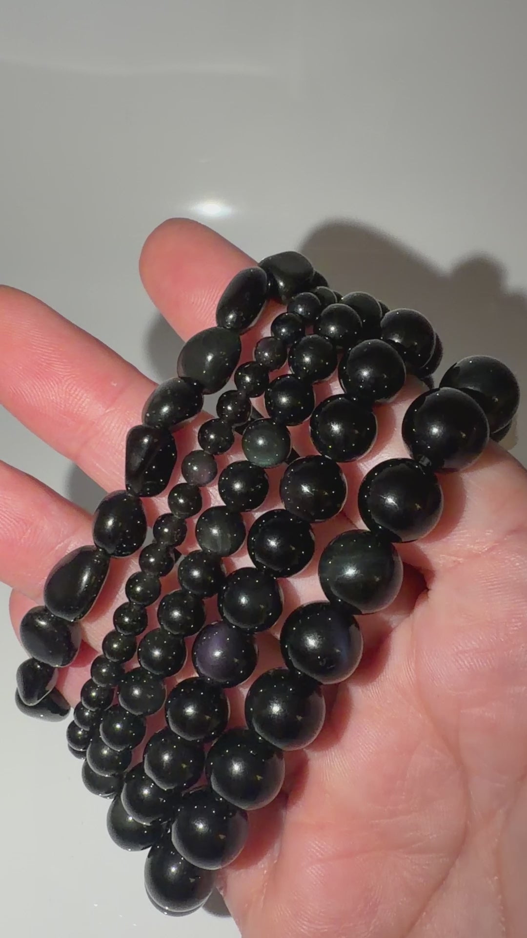 Video von den Kugelarmbändern aus Regenbogen-Obsidian mit irisierenden Farbringen in Violett und Grün.